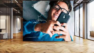 Close up of young phone addicted teenager using mobile cellular lay down on the sofa at home - happy technology millennal people with internet connection device  listening music with heaphones Wall mural