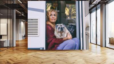 Cute adult woman sitting and relaxing on the door of her camper van with her two pug dogs. Best friends and friendship concept. Van life and travel road holiday life vacation. Modern female people Wall mural