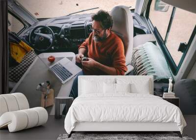 Digital nomad and travel wanderlust lifestyle people concept. One man viewed from above working on laptop and drinking coffee inside a modern camper van. Job and vacation lifestyle. Holiday and work Wall mural