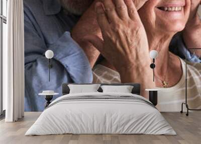 Elderly husband surprises his mature wife by covering her eyes with his hands and hugging her from behind. Their joyful and playful expressions reflect a happy celebration, whether a birthday  Wall mural