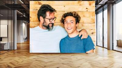 Father and son portrait - adult and young teenager generations smile and hug together with wooden background - youthful and mature ages concept Wall mural