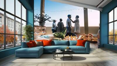 focus on a table full of fresh food fruits and other and friends ready to start the dinner together in friendship. home terrace with view on a blue sky in background.  friends having fun in outdoor  Wall mural