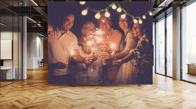 group of caucasian people friends with different ages celebrate together a birthday or new year eve by night outdoor at home. lights and sparkles  with cheerful women and men having fun in friendship Wall mural