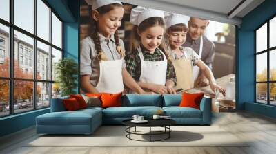 Group of children learning how to cook and prepare cookies all together in classroom. Chef student young child enjoy class having fun with food and raw ingredient to prepare meal in indoor kitchen Wall mural