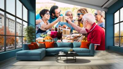 Group of different ages people celebrate and eat together in friendship outdoor at home - happy young, adult and senior have fun clinking and enjoying food on a wooden table - celebration  Wall mural