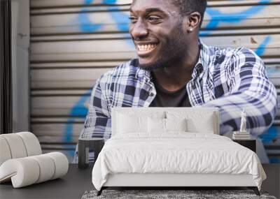 Handsome cheerful beautiful young black man african american smiling and having fun while sit and relax in the city with urban background. youthful concept for hipster style teenager boy Wall mural