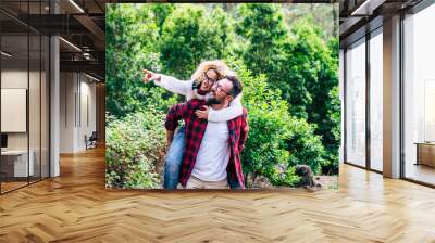 Happy adult couple enjoy the nature outdoor leisure activity together with man carrying cheerful beautiful woman with green forest in background - concept of happiness and love for people Wall mural