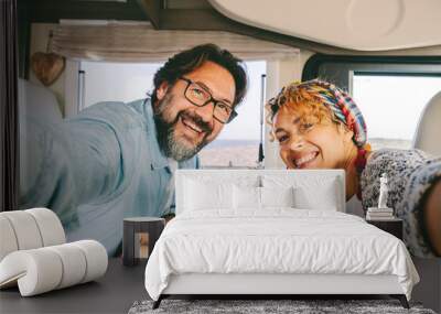 Happy and cheerful confident man and woman couple smile and have fun taking selfie picture inside a cozy modern camper van. Tourist and vanlifers people enjoy freedom happiness together on vacation Wall mural