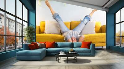 Happy and joyful adult woman lay down on the sofa in reverse position with legs up and head down smiling and having fun at home - middle age young lady active lifestyle laughing a lot on the couch Wall mural