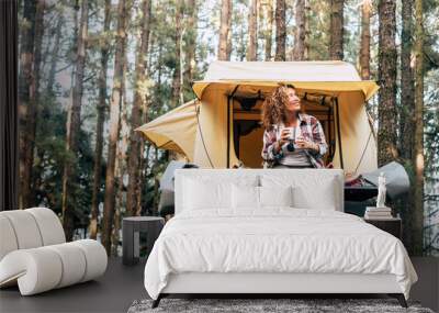 Happy hipster traveler people enjoying the alternative vacation - car with tent on the roof and beautiful young woman sit down outside looking at the forest around - outdoor activity Wall mural