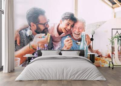 Happy people family concept laugh and have fun together with three different generations ages : grandfather father and young teenager son all together eating at lunch Wall mural