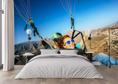 Happy tourist doing paragliding sport activity in outdoor leisure active lifestyle. Cheerful adult woman doing selfie picture flying on a paraglyde in summer holiday vacation. Freedom joyful people Wall mural