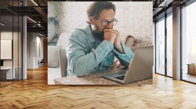 Man looking a display notebook concentrated to find a solution. Freelance people and business lifestyle in alternative house apartment office. Smart working lifestyle. Mature using laptop computer Wall mural