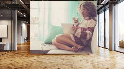 middle age beautiful model woman sitting at home on the sofa reading an ebook on tablet connected with internet. office work indoor alternative lifestyle with independent day and enjoying life Wall mural