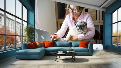 Modern people smart working at home with computer laptop and internet connection and dog love lifestyle - new job and happy life for woman hugging her puppy in the office in working activity alone Wall mural