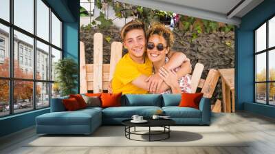 mother and son hugging with smile and enjoy leisure time together with love. family teenager boy 14 years old and mom 43 have fun sitting on a wodd bench outdoor in a sunny day. happiness family Wall mural