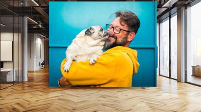 My best friend dog concept with funny scene adult man with beard and pug dog kissing him on the face - people and animals have fun and love together in friendship Wall mural