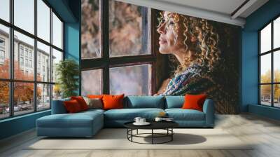 One alone woman standing at home near the window looking outside and thinking. Single female people lifestyle. Waiting friends and thoughts. Young lady indoor leisure. Side portrait of middle age Wall mural