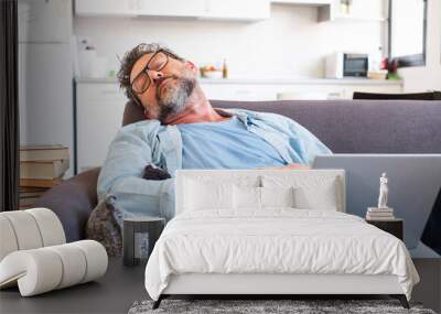 One man fall asleep at home after laptop work leisure activity on the sofa in the afternoon. Modern tired male people sleep holding computer on the legs Wall mural