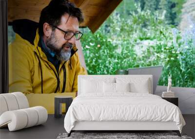 One man using phone outdoors in modern desk workplace with laptop. Outdoors leisure activity and working people. Nature around. Yellow jacket. Messaging with cellular and roaming connection online Wall mural