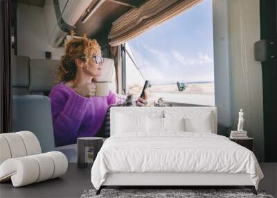 One tourist woman admire the beach inside her modern camper van and use mobile phone. Summer transport holiday vacation people with motor home. Alternative home and lifestyle. Vanlife lady leisure Wall mural