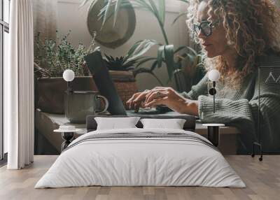 One woman at home using laptop in green mood color background and ambient. House indoor garden in background. Attractive female people use computer for work or surf the web in indoor leisure lifestyle Wall mural