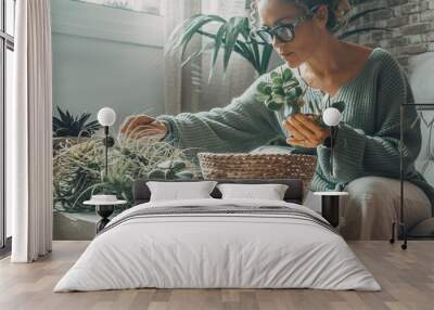 One woman enjoy indoor gardening at home working with plants. Leisure activity at home. Female with eyeglasses work with green nature inside house. Real. life people in apartment. Green moody colours Wall mural