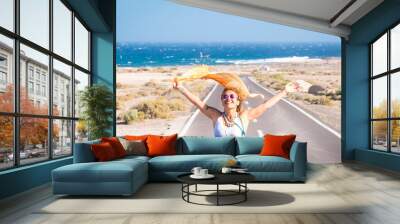 one young woman enjoying and having fun in their vacations outdoors - female person in freedom concept and lifestyle with a car in the middle of the road woth the ocean or sea at the background Wall mural