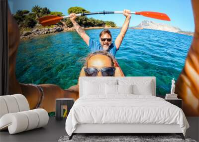 Overjoyed couple of caucasian adult tourist man and woman taking selfie picture inside a kayak canoe with blue clean sea ocean water and coastline in background. Travel and summer holiday vacation Wall mural