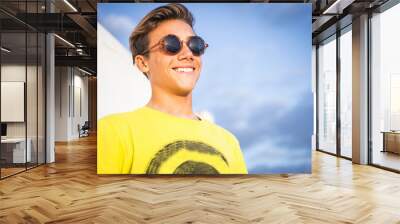 Portrait of handsome young guy boy smiling with sun in front - outdoor leisure activity and happy beautiful people with sunglasses, yellow and blue color backgorund Wall mural