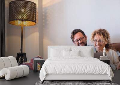 Portrait of two people man and woman enjoy technolofy connection toether with laptop and phone smiling and watching the computer - happy cheerful couple at home sitting on the sofa at work Wall mural