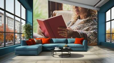 Relaxed adult lady reading a book sitting on the chair at home with outside view. Concept of female people happy lifestyle living alone. Attracvite woman studying indoor Wall mural