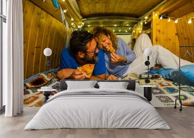 Romantic people adult young couple in love enjoy the little tiny house inside an old restored vintage van eating pizza together and having fun - concept of travel and alternative vacation Wall mural