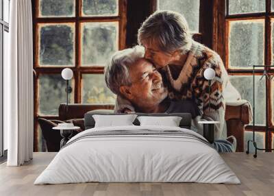 Senior people at home in love kissing and caring each other. Happy relationship mature man and woman together. Old male sitting on the couch and aged woman hugging him with care Wall mural