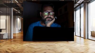 Stressed and worried man work by night on laptop computer - online social media life and stress for job people - adult male with glasses working with technology at home or office Wall mural