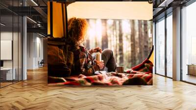 Travel and relax destination people concept - blonde curly woman lay down inside the tent with backpack and coffee - forest and sunlight in backgorund - adventure and alternative wanderlust lifestyle Wall mural