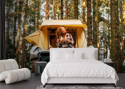 Travel and wanderlust lifestyle concept with happy lonely adult woman sit down on the roof tent car vehicle with wood forest in background enjoying nature and outdoors vacation Wall mural