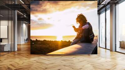 Trendy woman enjoying the phone connection during a coloured beautiful sunset on the coast - outdoor leisure activity for traveler modern people Wall mural