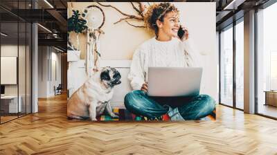 Woman smile and talk at the phone with her best friend dog sit down near her. Modern people smart working lifestyle using computer and enjoying animal friendship with a pug. Concept of couple Wall mural