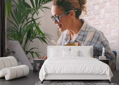 Woman working at home office table eating healthy food in a bowl. Independent female people lifestyle, Alternative job occupation using laptop computer and online opportunity. Modern worker business Wall mural