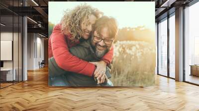 Young adult mature couple in love hugging and smiling with romance expression on face. One man carry woman in piggyback on his back. Female bonding male in outdoor leisure activity together. Happiness Wall mural