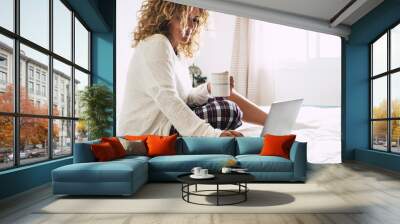 Young adult woman working at home in the bedroom during morning breakfast work activity - quarantine for coronavirus health emergency - happy female with computer laptop and coffe cup - white light Wall mural