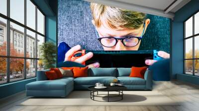 Young and concentrated caucasian child gamer with portable device playing with technology games internet connected with friends - video game addiction to console and obsession Wall mural