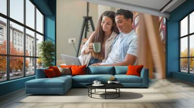 Young boy and girl together at home enjoying laptop computer sitting on the floor smiling and laughing - new life married people in love and relationship have fun watching online internet web Wall mural