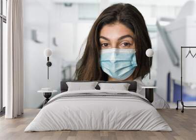 A brunette scientific researcher in a surgical gown and mask. In the background the blurred medical laboratory. Wall mural