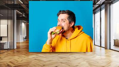  white guy in yellow hoodie eating hamburger on blue background Wall mural