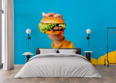 Male hand in yellow clothes hold hamburger on blue background Wall mural