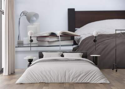 pile of books, opened notebook, candles and lamp on the table near bed in the bedroom Wall mural