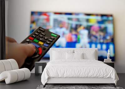 Close-up macro of man's hand with TV remote control watching a soccer match Wall mural