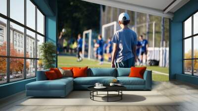 boy standing and looking at football players, blue football players uniform, football field, game, childhood, child, baby, kid, Wall mural